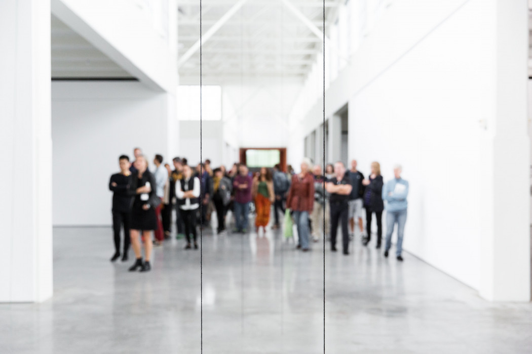 A group of people walking in large white gallery. They appear blurry, as if the photo was taken in a mirror.