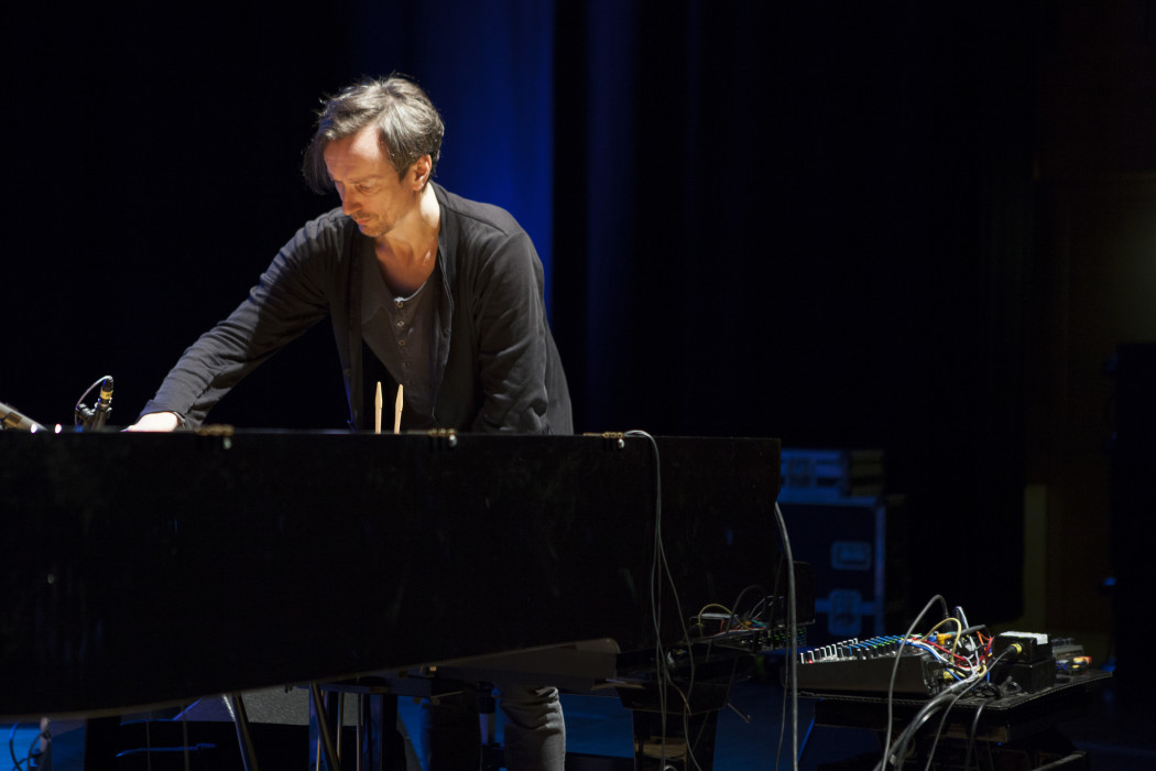Hauschka stands over a grand piano, with wires coming out form the instrument and connects to a remix board.