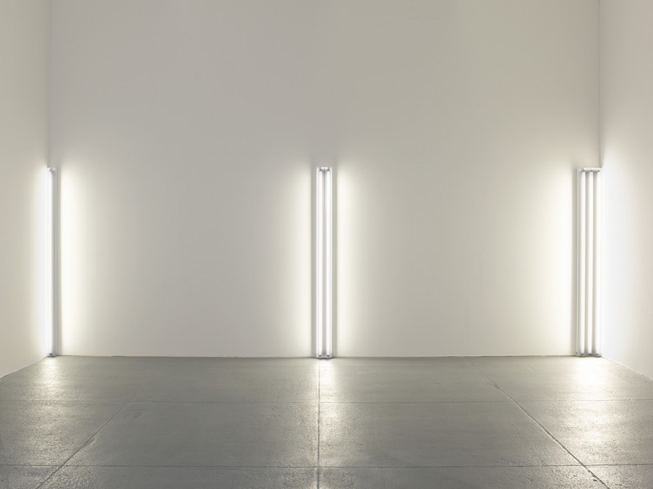 Three sets of fluorescent white tubes installed vertically along a wall, one tube at left corner, two in the middle, three at right corner.