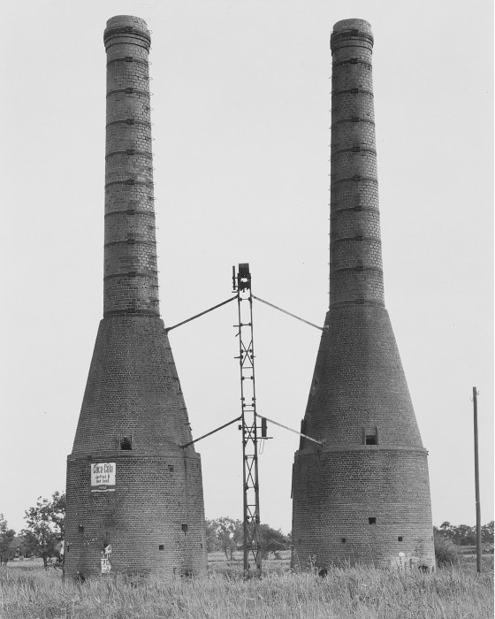 Black-and-white photograph of two brick towers with thick cylindrical bases, conical mid-sections, and thin cylindrical tops.