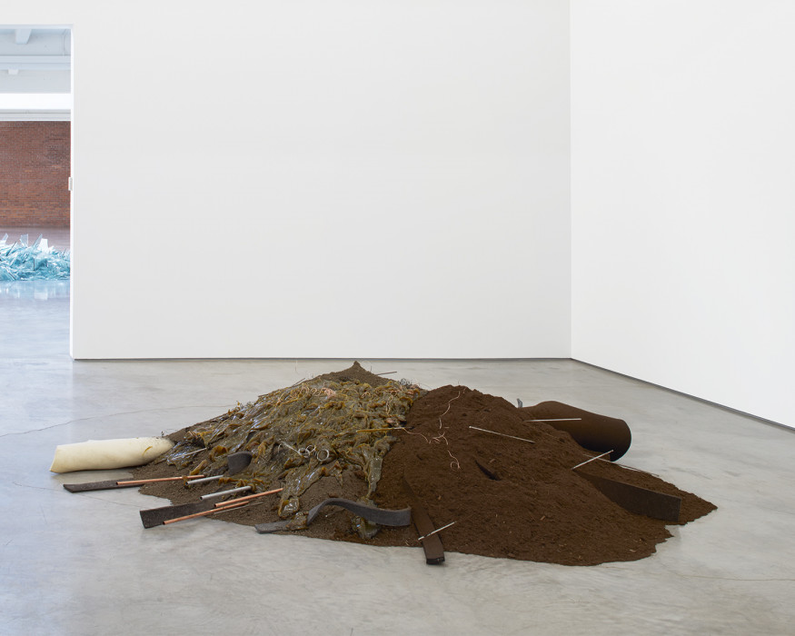A pile of dirt and moss is strewn with strips of felt and metal rods above a cement floor.