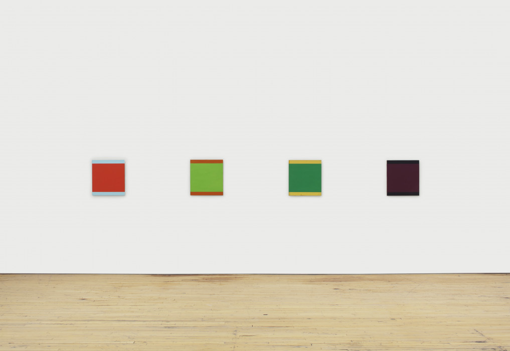 Four multicolored squares hang in a row on a white wall.