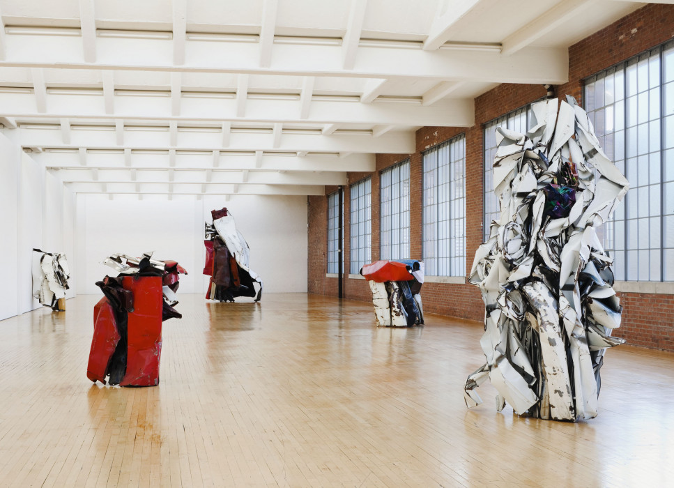 Five immense, crushed autombolie steel forms of varying height, breadth, and color sit throughout the large airy hall. The closet form is larger-than-life size and made of white-grey crushed automobile steel.