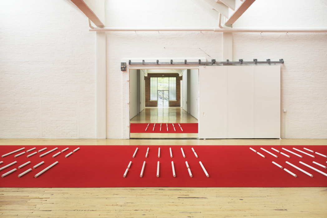 A series of white hexagonal poles laid horizontally on a red carpet.