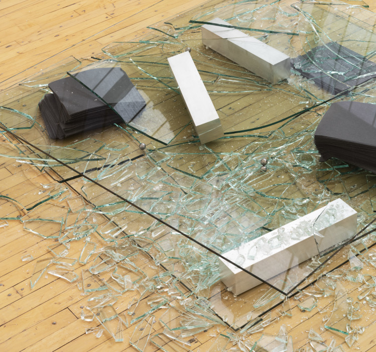 Smashed sheets of glass on top of stacks of purple felt and white rectangular blocks.