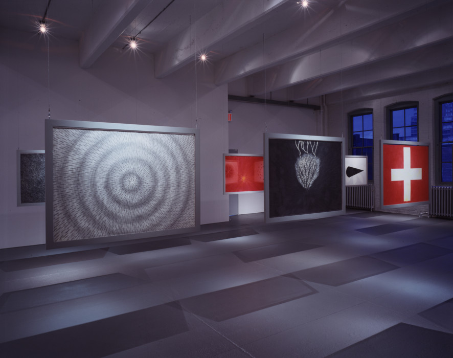 Two rows of three abstract images in red, gray, black, and/or white hang in silver frames from the ceiling in a dark room.