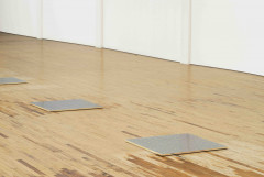 A square silver plaque featuring a grid of gold dots lies flat on a wood floor.