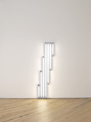 Seven fluorescent-white, tubular lights positioned against a white wall at varying heights beginning with the shortest bulb.