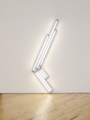 Seven fluorescent-white, tubular lights positioned against a white wall and placed at an angle, four of which are shorter bulbs slanted toward the floor and three of which are longer bulbs slanted upward.