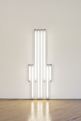 White fluorescent tubes are mounted in the shape of a tower on a wall.