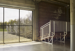 Outdoor bleachers on gravel are framed by a large glass window, while another set sit inside a large sunlit industrial space.