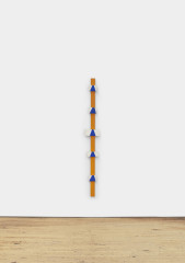 A tall, narrow orange pole with small white and gray rectangles dotted on its surface hangs on a white wall.