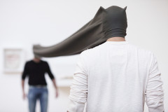 Two people stand facing each other at a distance with a long, stretchy gray hood stretched between their two heads.