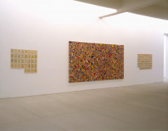 A large horizontal mutlicolored artwork hangs in between two groups of multiple framed, small color drawings on a white wall.