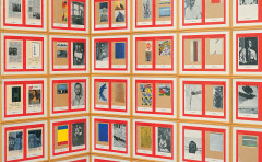 Paper works installed in a locked grid on a wall, each with a bright red background with two tan pages of a notebook, each with uniquely collaged images, texts, pages, postcards, or handwritten notes.