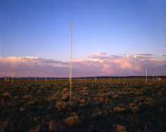 Tall silver poles sticking up out of a grassy landscape, with purple storm clouds in the sky.