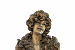 A bronze bust of a young woman with long, voluminous waves gazes outward with head tilted to the right and a small open-mouthed smile. The rightside of the chin shows signs of damage