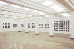 Several grids of square-format photographs hang in a white industrial space.