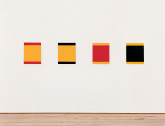 Different square-shaped, color-blocked paintings of red, marigold, and black hang on a white wall.