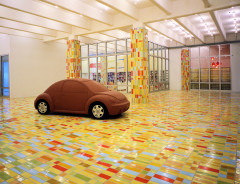 A brown full-scale model of a Volkswagen New Beetle sits in a room with colorful mosaic floor and column tiles.