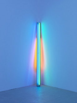 A blue fluorescent tube leans on the corner of a wall, reflecting red and orange tones behind it. 