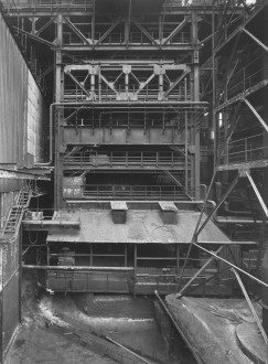 Black-and-white photograph of a tiered metal structure with railings, platforms, and diagonal support beams.