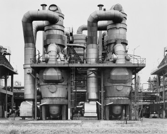 Black-and-white photograph of factory with curving cylindrical tubes, tanks, and other protuberances