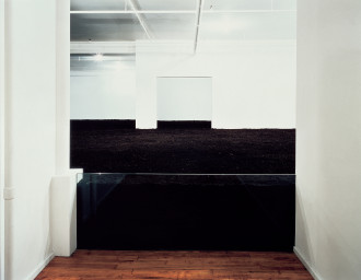 A white room filled halfway with dirt, entry is blocked by a glass barrier.