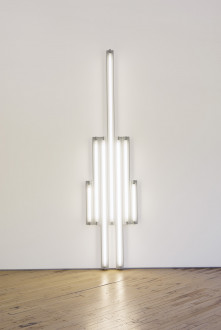 White fluorescent tubes are mounted in the shape of a tower on a wall.