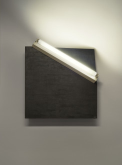 A white fluorescent tube lays diagonally across a black square mounted on a wall. The upper right corner of the square is bent backwards.
