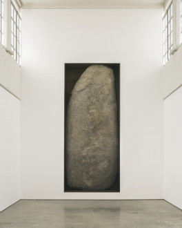 A large gray-brown rock sits upright in a rectangular cutout of a white wall.