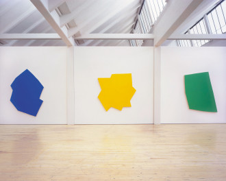 Three large wall-mounted polygons in different, irregular shapes, one bright blue, one yellow, and one green.