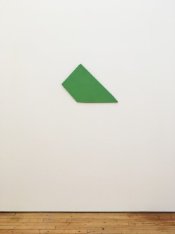 A flat, green trapezoidal object affixed to white wall.