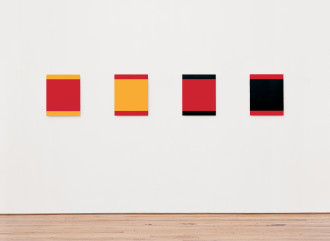 Four multicolored squares hang in a row on a white wall in a large room.