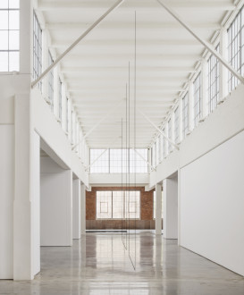 Dark threads are hung from the ceiling and run along the floor at 90-degree angles in a bright corridor in an industrial space.