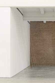 Five white threads, spaced evenly apart, are suspended between the top of the wall and the concrete floor.