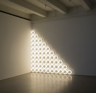 A triangle composed of white fluorescent circular tubes is placed on a white wall. 