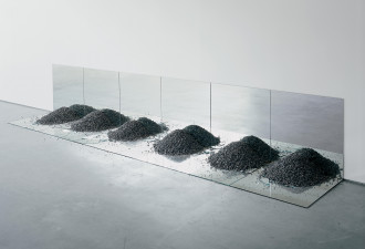 Six pairs of mirrors set in right angles at the junction of the wall and floor with piles of gravel atop the cracked floor mirrors.