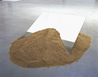A mound of sand on a concrete floor with a rectangular mirror sticking out of it.