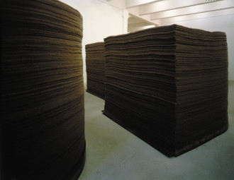 Three large stacks of brown felt: a central rectangular stack, a circular stack that extends toward the left, and another rectangular stack only partially visible in the back between the two other stacks.