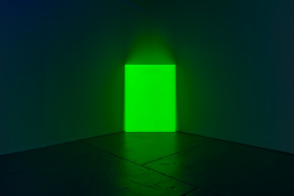 A vertical fluorescent green rectangle leans against the corner of a dark room.