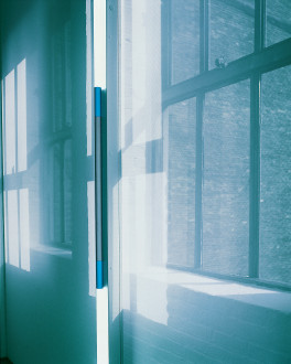 A scrim and vertical neon light in front of a window, all steeped in a blue haze.