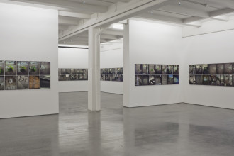 Two flush rows of photographs hang on every wall of a white gallery space.