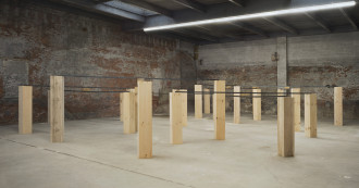 A room filled with upright planks of wood of varying heights, some connected on the top by black strips.